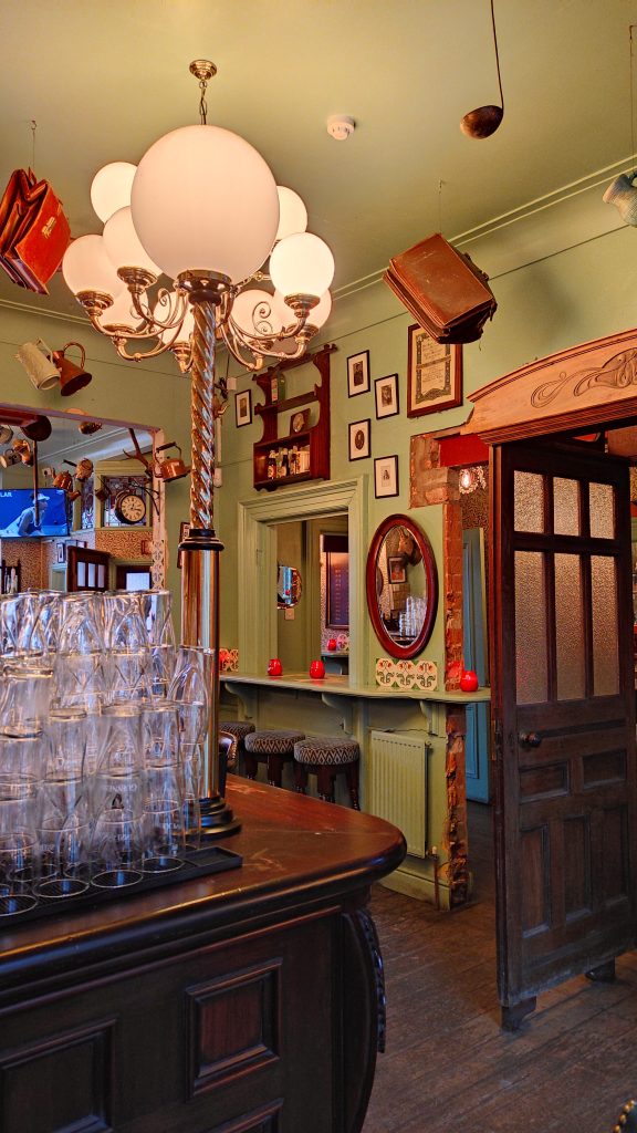 5 Pubs À Ne Pas Manquer Lors De Votre Prochaine Visite À Liverpool 8 Intérieur d'un pub avec verres sur le comptoir et portraits au mur