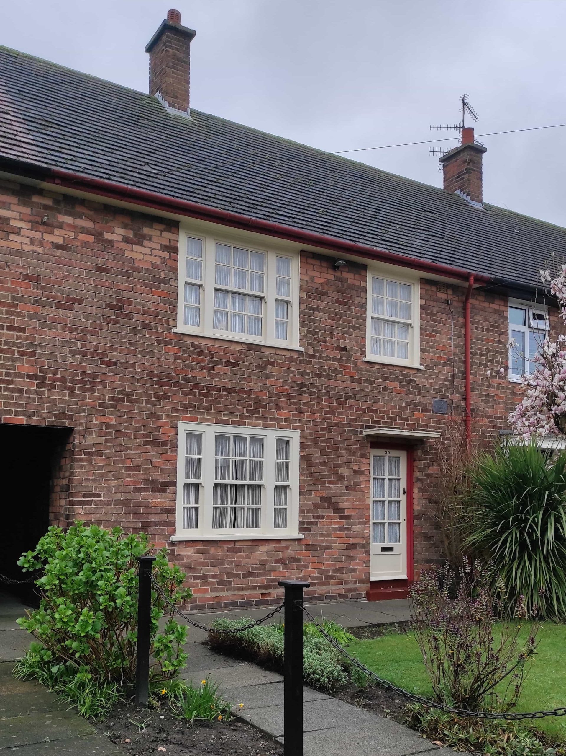 Liverpool et les Beatles : musées, visites, et lieux emblématiques à ne pas manquer 5 Maison d'enfance de Paul McCartney. Maison en briques rouges aux fenêtres blanches avec allée goudronnée qui mène vers une porte rouge et blanche.