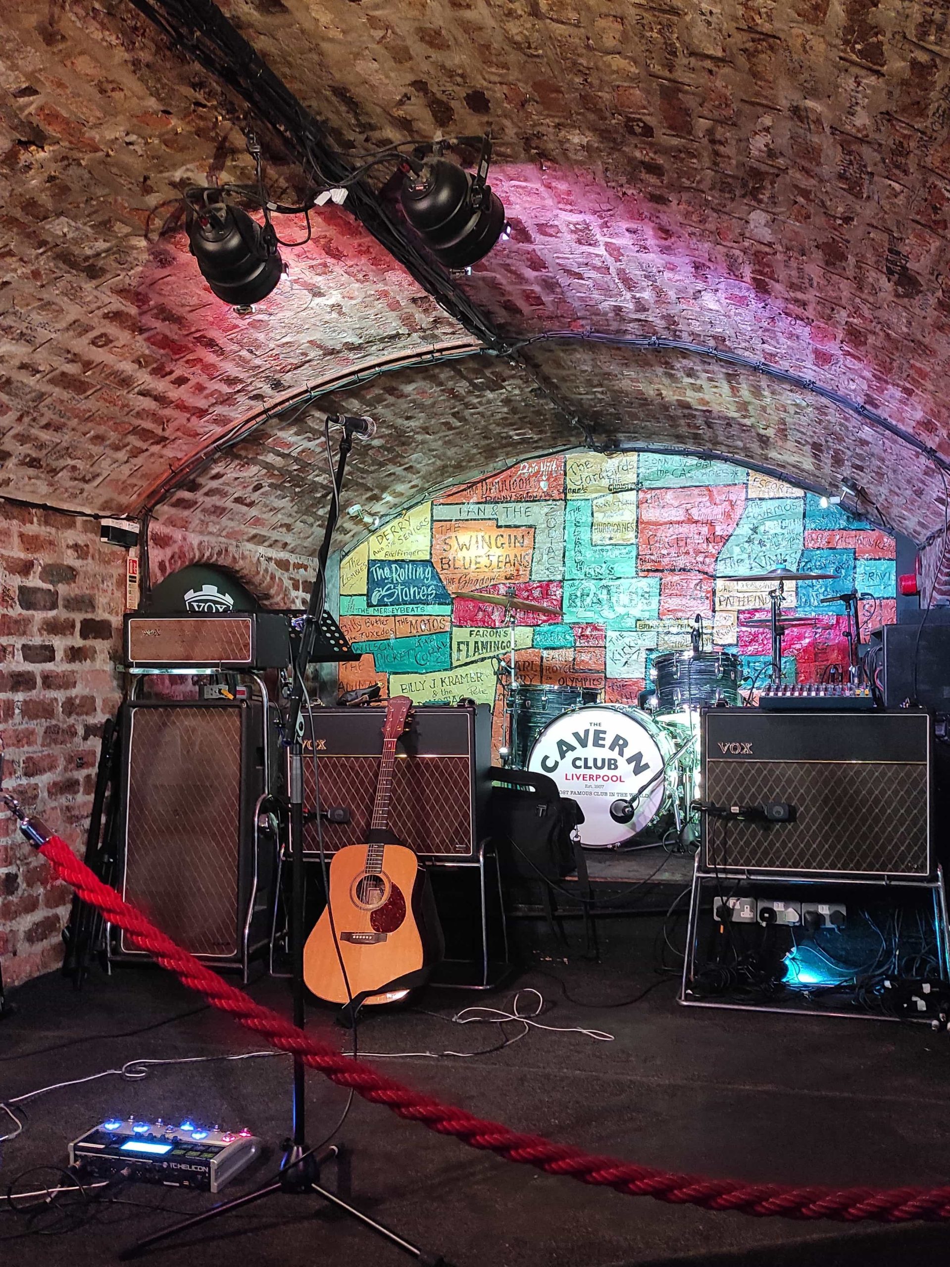 Liverpool et les Beatles : musées, visites, et lieux emblématiques à ne pas manquer 3 scène du club cavern avec mur de toutes les couleurs bariolé et instruments devant avec guitare, batterie et amplificateurs