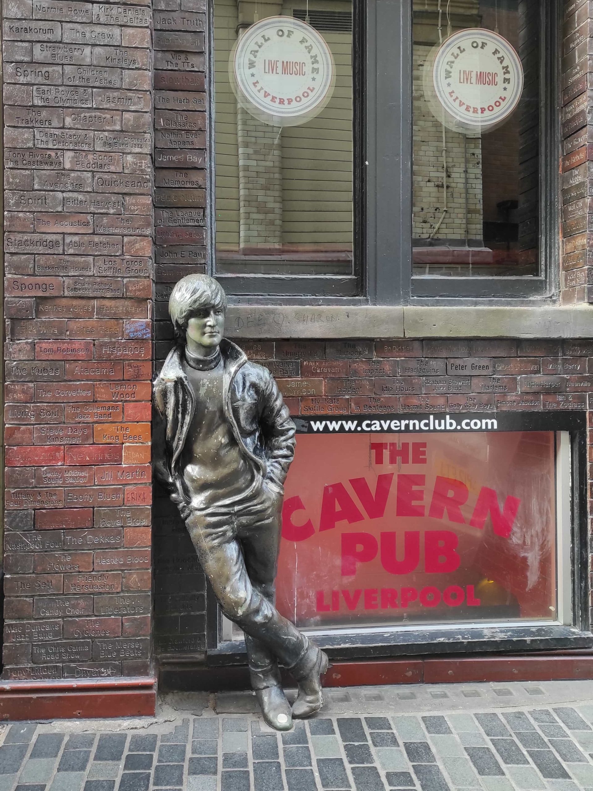 Liverpool et les Beatles : musées, visites, et lieux emblématiques à ne pas manquer 12 Statue de John Lennon devant mur en briques et enseigne du Club Cavern dans Matthew Street