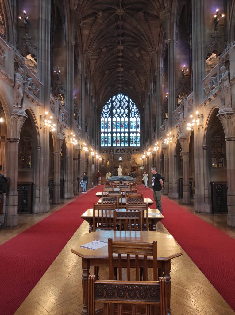 4 musées à Manchester à découvrir absolument sans débourser un centime 18 Salle de lecture dans une nef avec colonnes, plafond vouté et grand vitraux. Au centre sont alignées des tables et des chaises en bois.