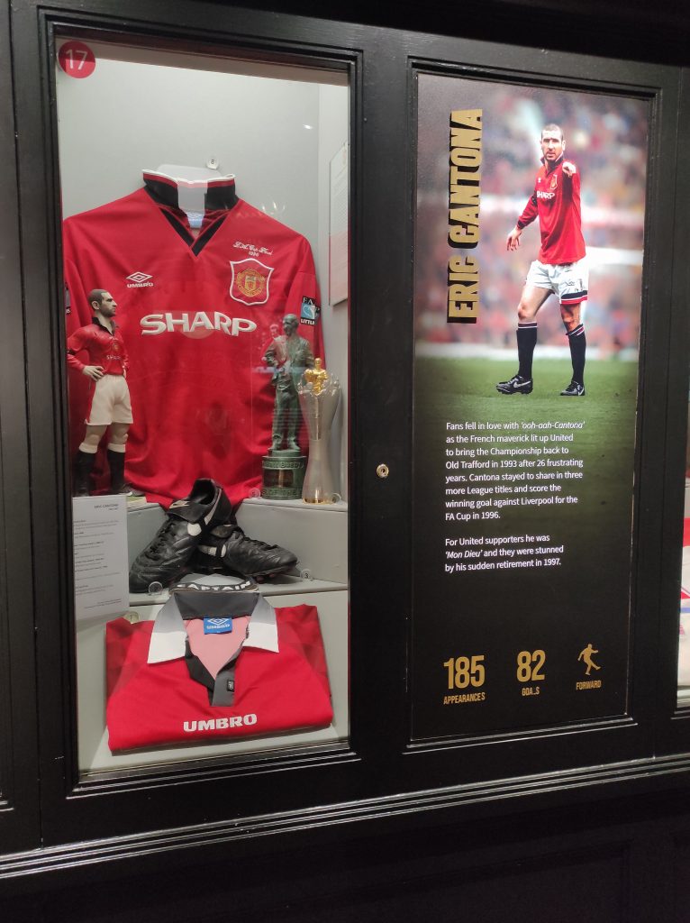 Visiter Old Trafford à Manchester : notre retour d’expérience et conseils pour vous organiser 7 vitrine à l'effigie d'Eric Cantona avec figures, maillot, chaussures