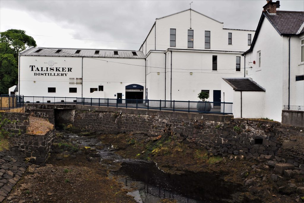 Visiter une Distillerie en Écosse : Tout Ce Qu’il Faut Savoir 4 Vue éloignée de la distillerie Talisker sur l'Ile de Skye. Bâtiment blanc avec enseigne sur le côté gauche
