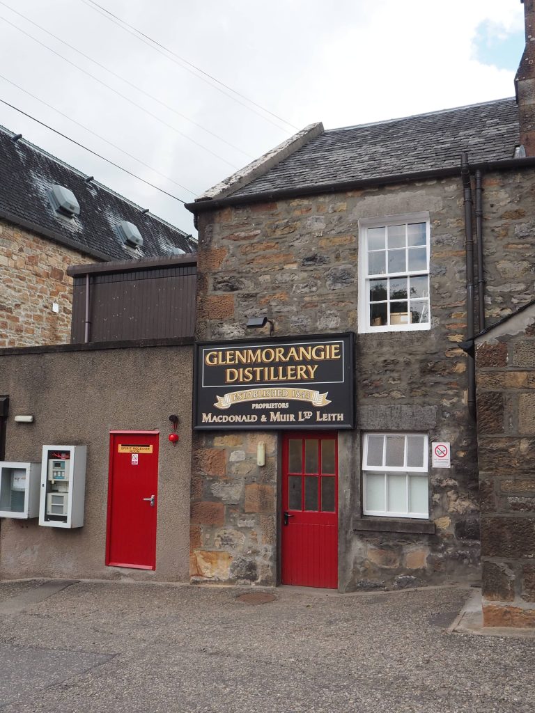 Visiter une Distillerie en Écosse : Tout Ce Qu’il Faut Savoir 2 Bâtiment d'accueil en pierre et ardoise de la distillerie Glenmorangie avec portes rouges et fenêtre blanches